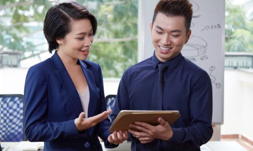 Two business partners standing together and discussing some presentation on digital tablet while standing at office