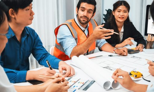 Diverse group of civil engineer and client working together on architectural project, reviewing construction plan and building blueprint at meeting table. Prudent
